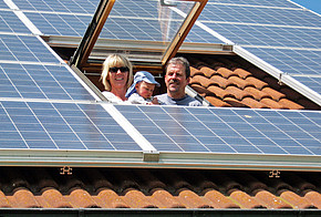 Photovoltaik-Dachfenster Solarmodule auf einem Dach mit Dachfenster, aus dem Frau, Baby und Mann herausschauen