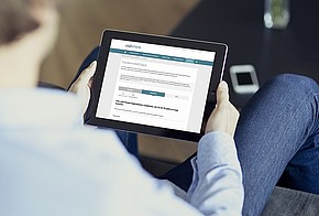 Mann sitzt auf der Couch mit einem Tablet und schaut sich den Fördermittelcheck auf www.co2online.de an.