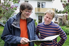 Energieberater mit Mappe und Eigentümer im Garten hinter dem Haus